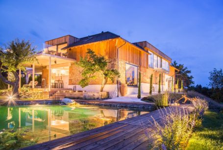 Das Loft bei Nacht mit beleuchtetem Naturpool und moderner Architektur bei Dämmerung.